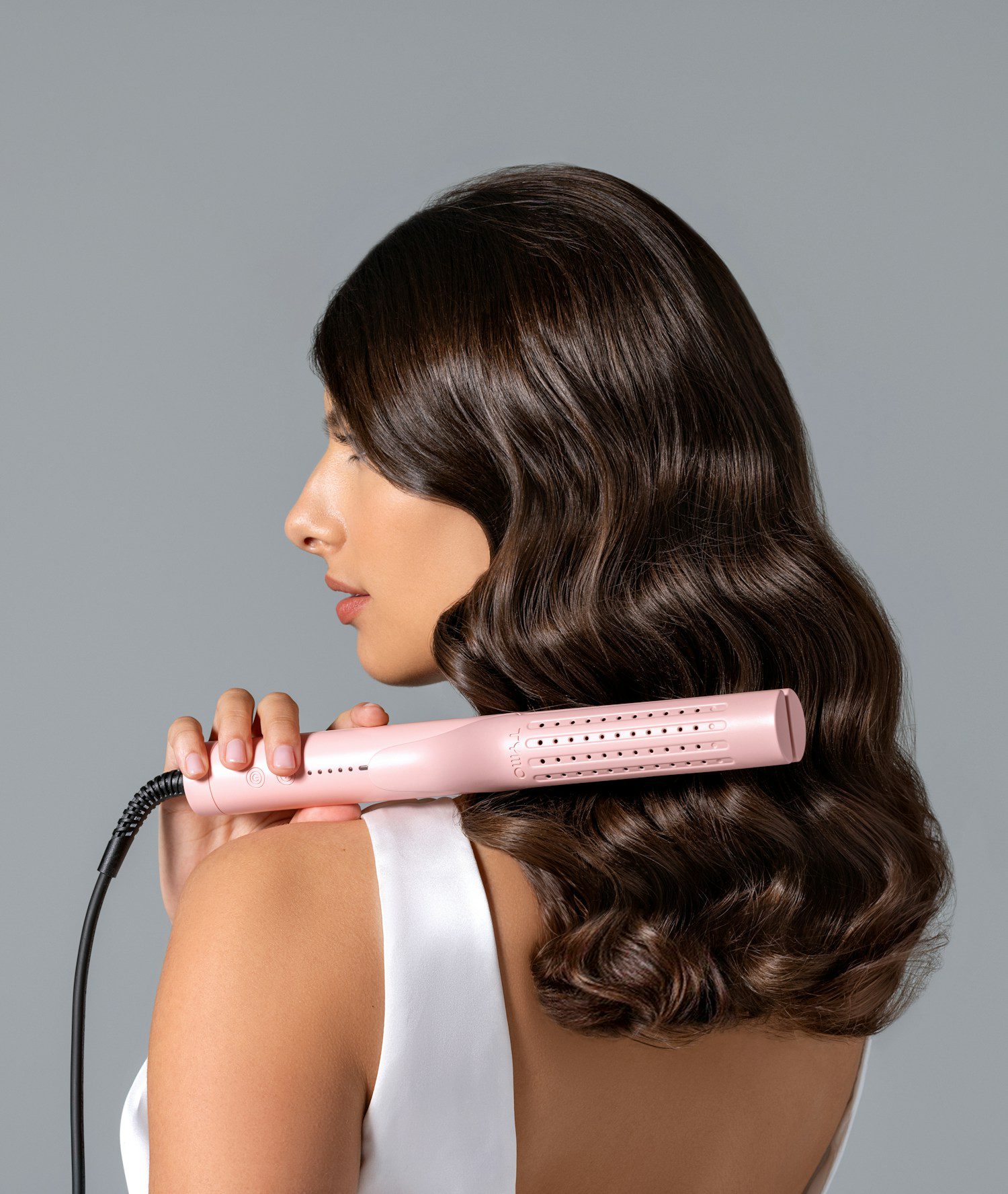 Een volwassen vrouw brengt haar bruine krullen in model met een haarstyler