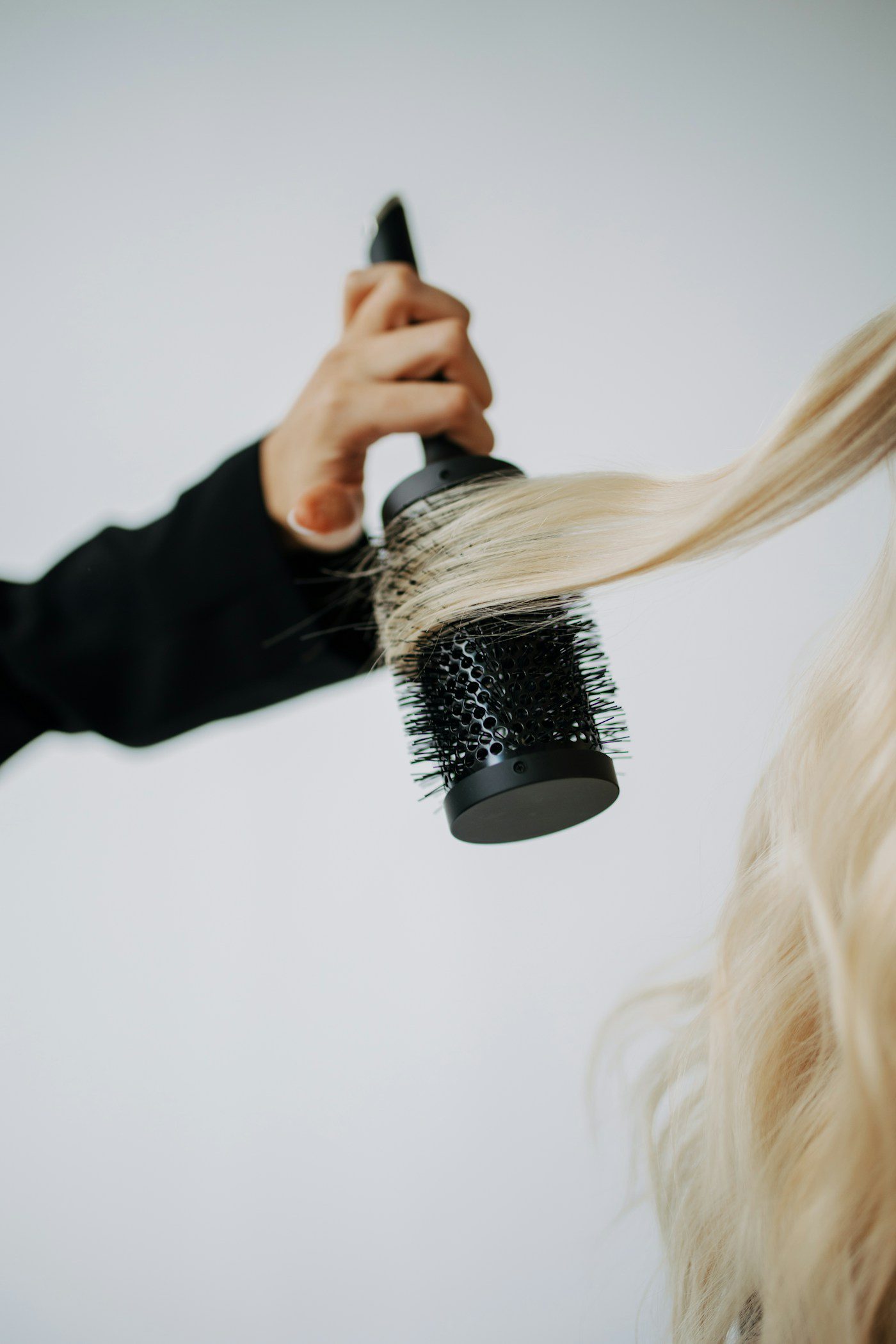 Een stylist modelleert blond haar met een ronde borstel